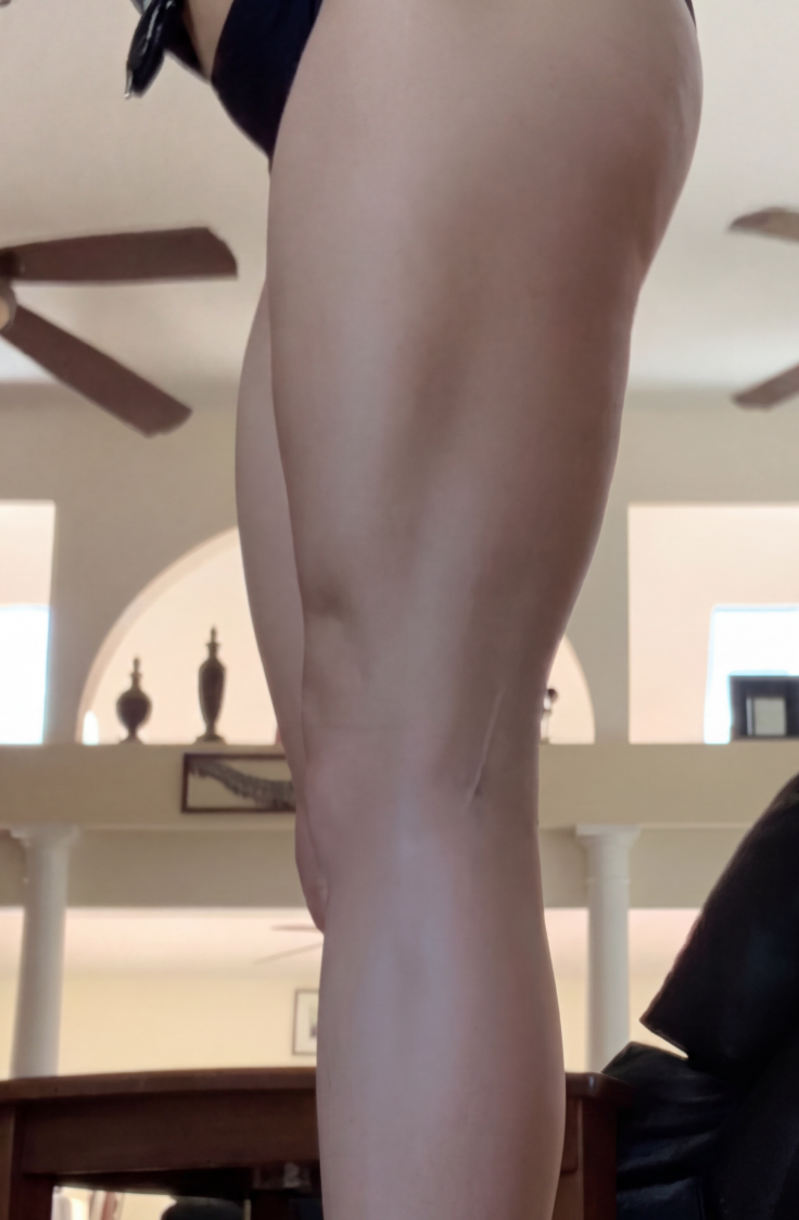 A low-angle side view of a person's thigh and leg in black bikini bottoms indoors.