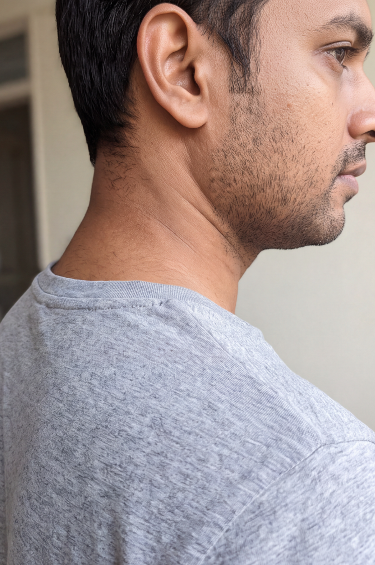 A close-up, side profile of a man's neck showing stubble, wearing a grey crewneck t-shirt.