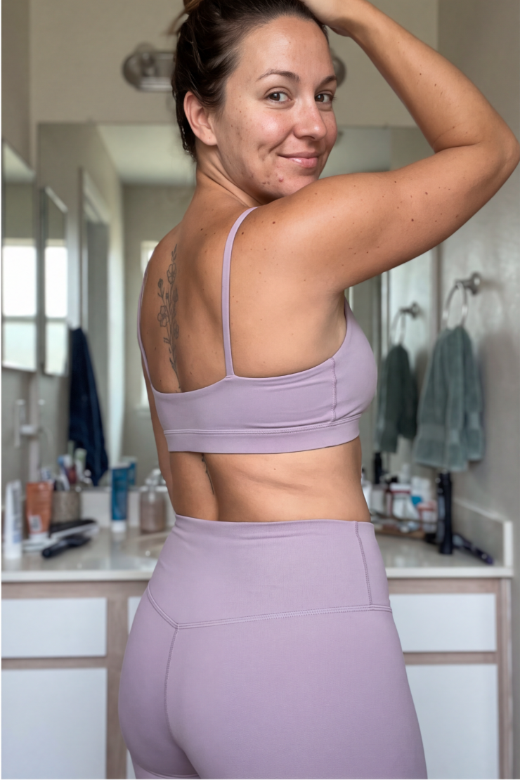 A woman in a lavender workout set looks over her shoulder, showing a tattoo on her back.