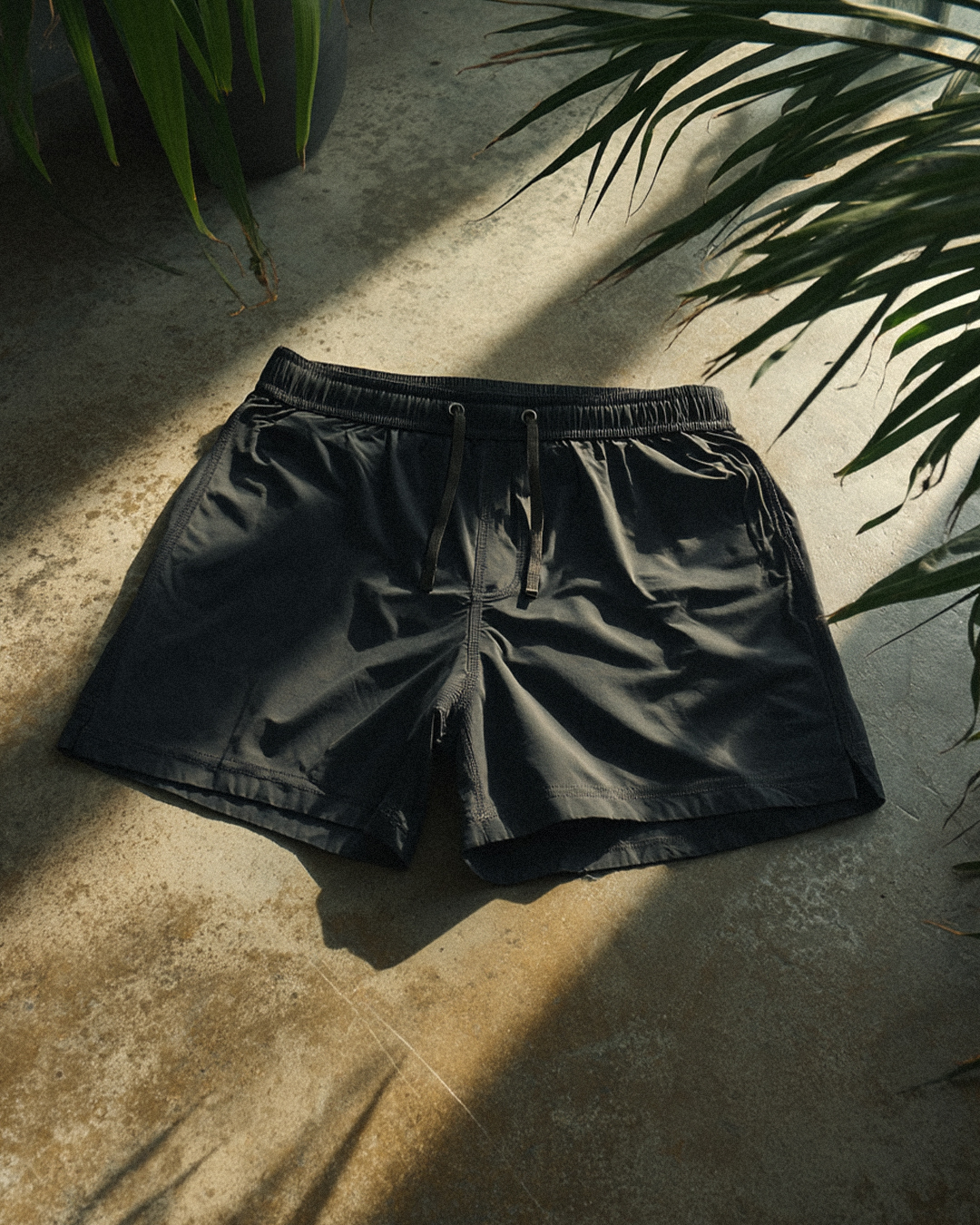 Black shorts on a concrete floor with plant shadows.