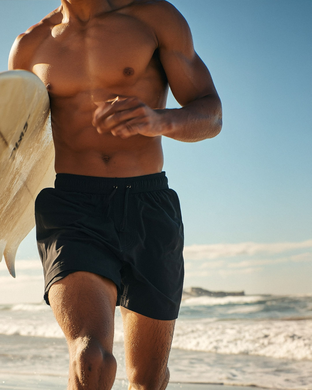 Man running on beach holding a surfboard.