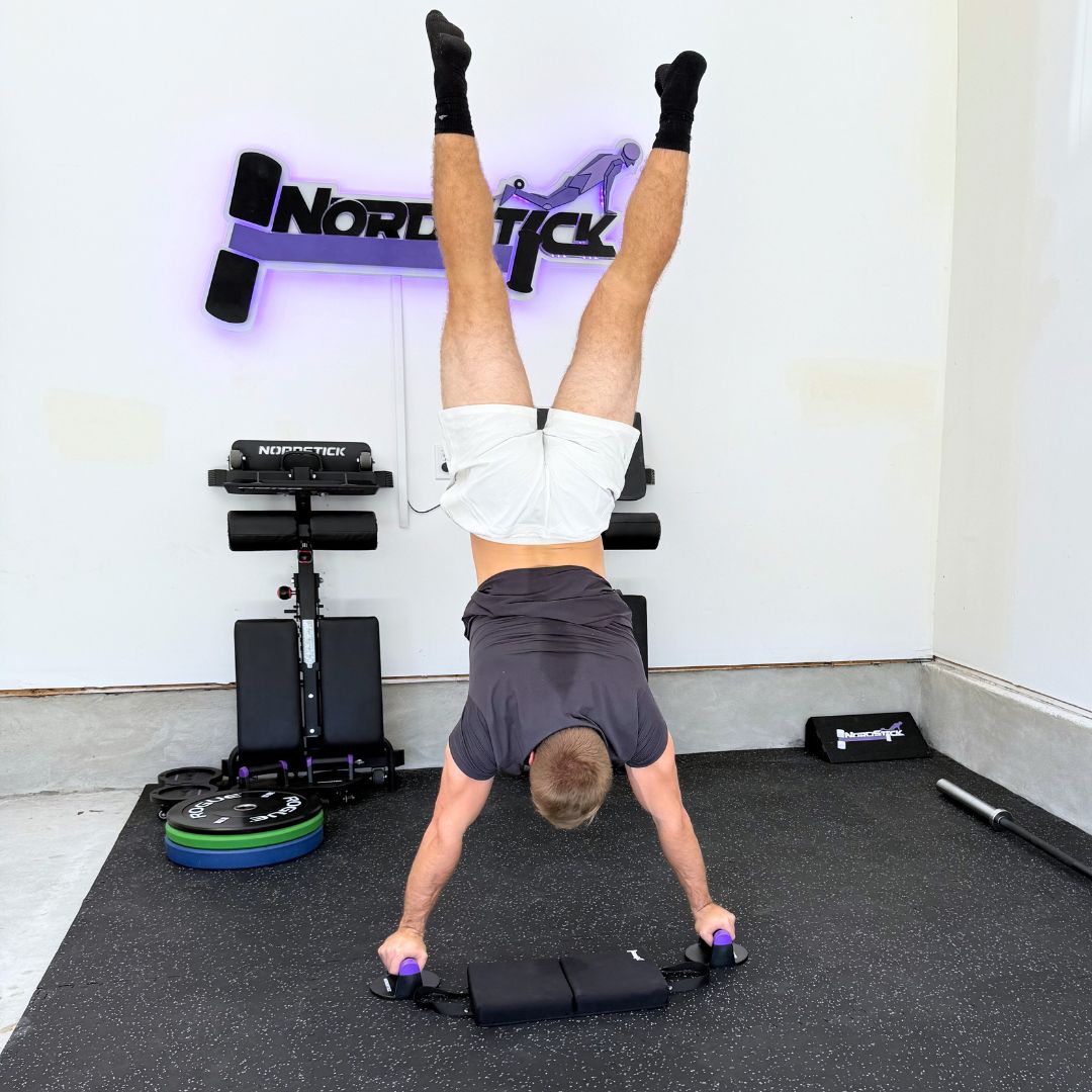Person doing a handstand on exercise equipment in a gym setting.