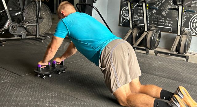 Person exercising with push-up bars on a gym floor.