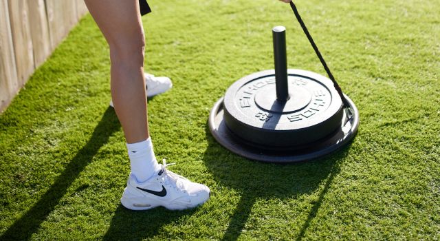 Person pulling a weight sled on grass with a rope.