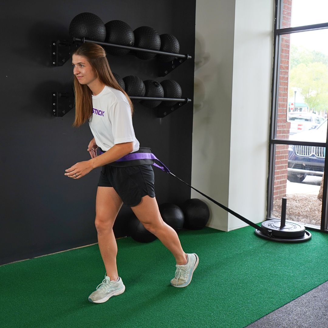Woman training with resistance sled indoors on green turf.