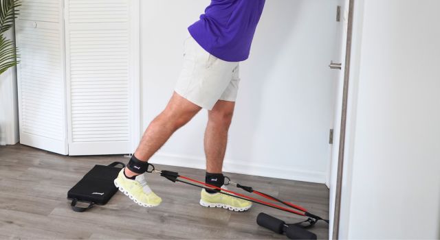 Person exercising with resistance bands attached to ankles indoors.