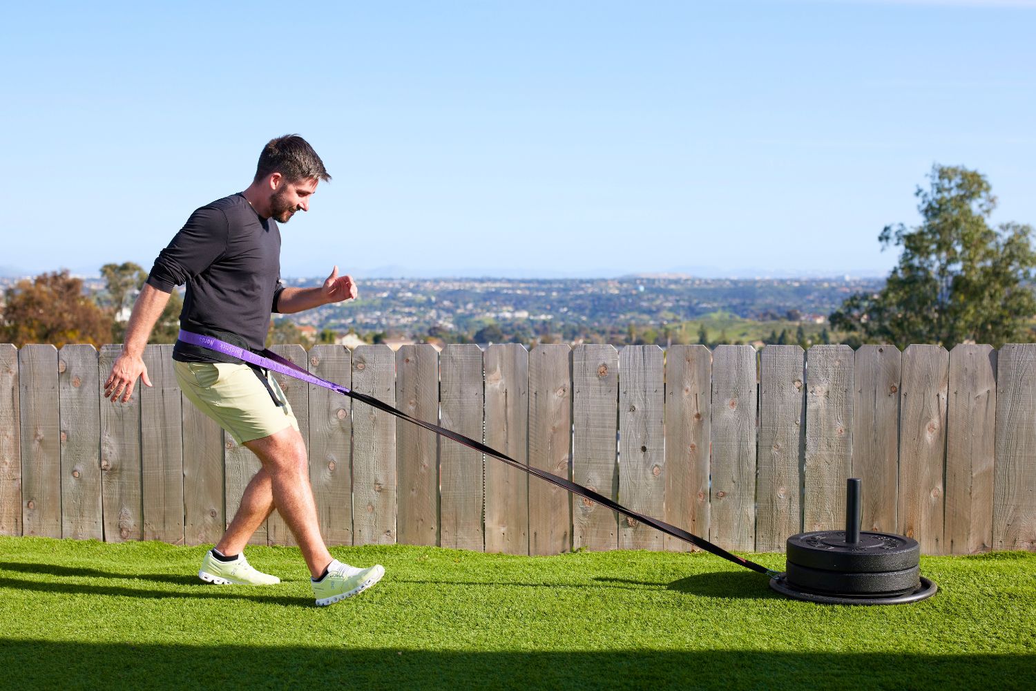 Man pulling a weighted sled outdoors on a grassy area.