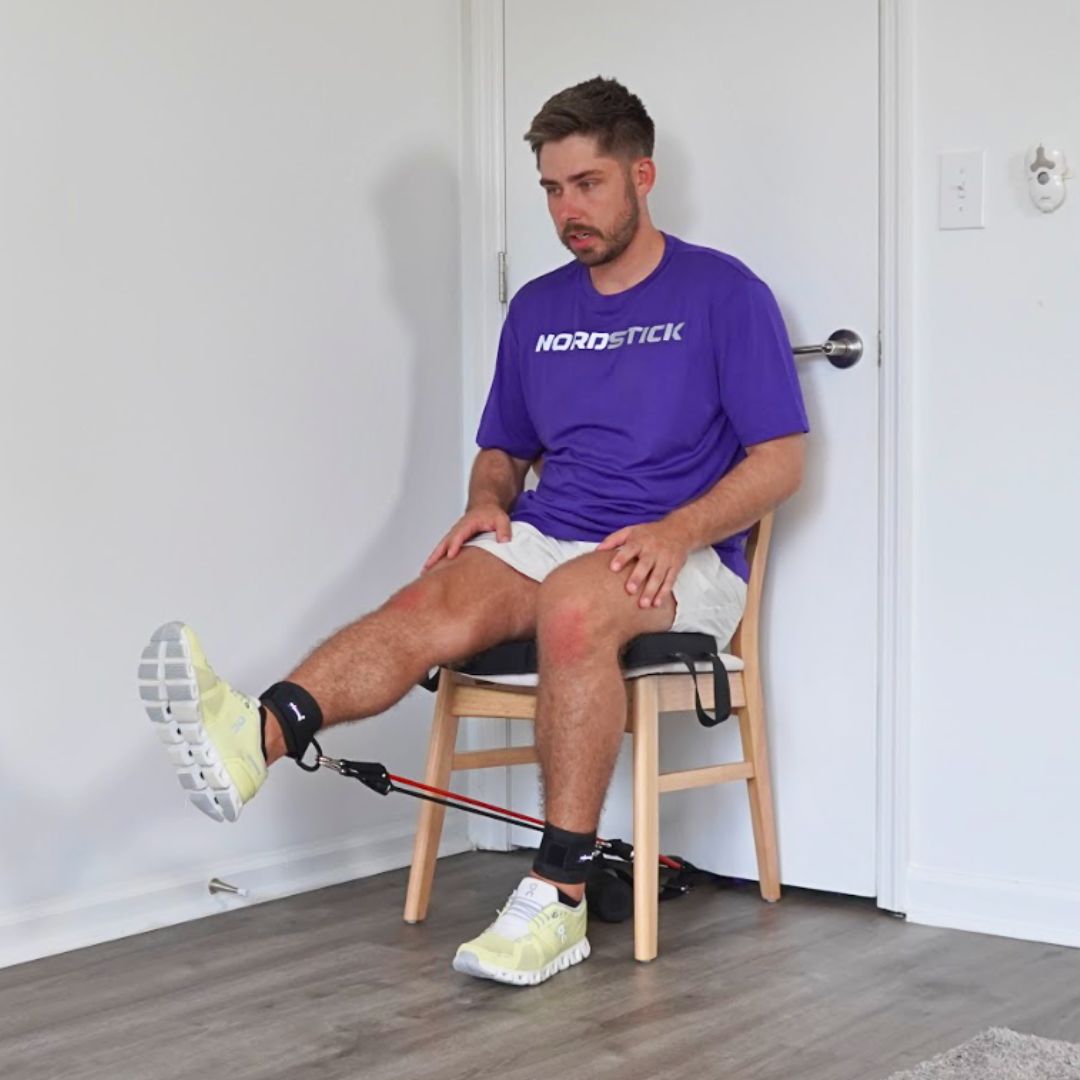Man sitting on a chair using resistance bands for leg exercise.