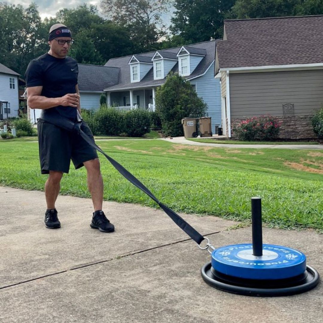 Man pulling weighted sled on a suburban sidewalk.