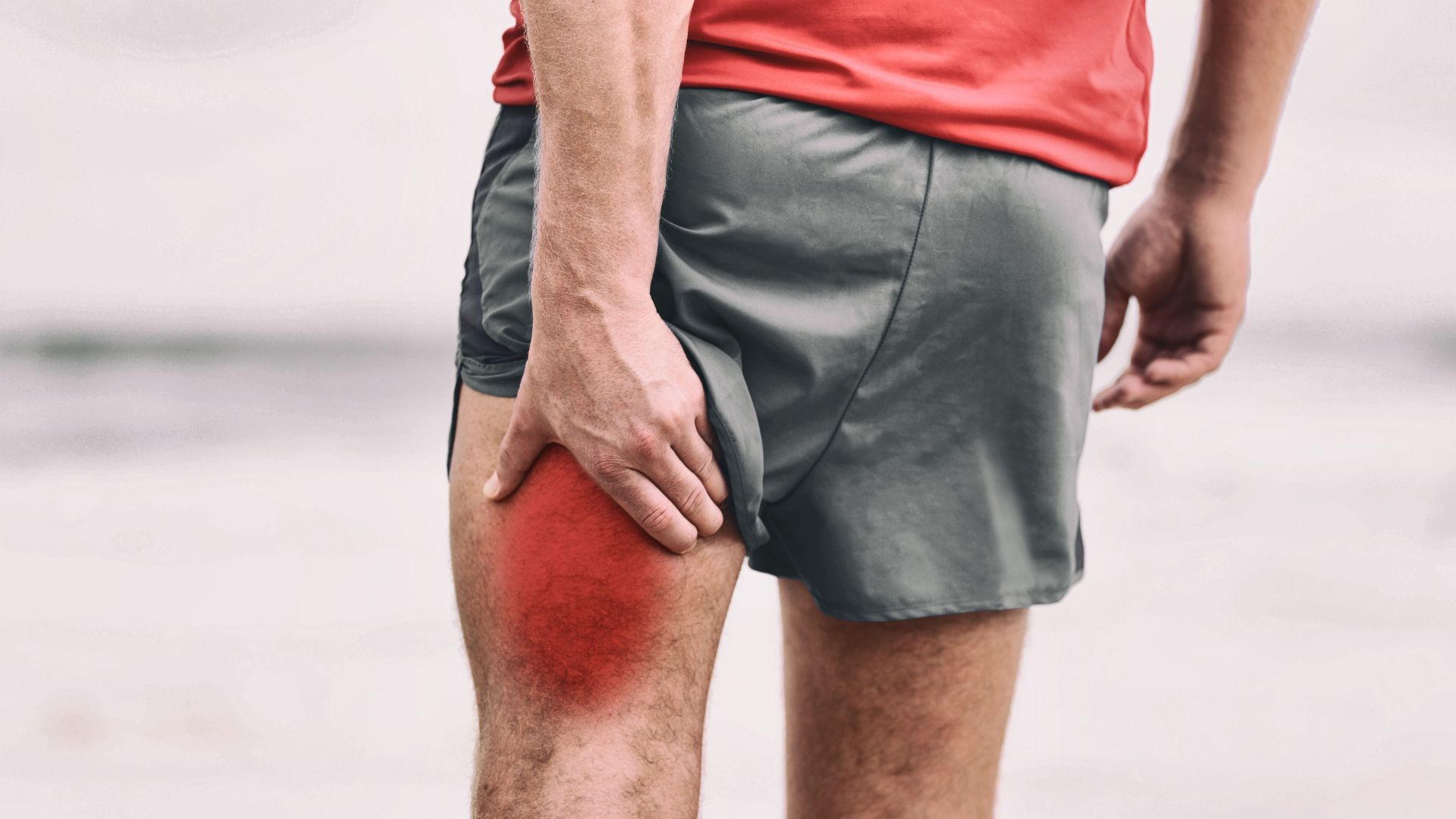 Person holding their thigh with a red highlighted area, wearing shorts and a red shirt.