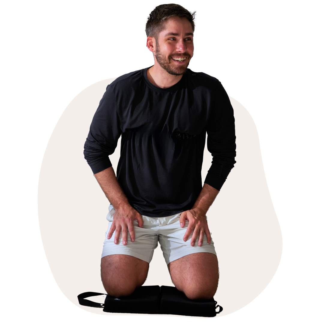 Man kneeling on a cushion, smiling, wearing a black shirt and white shorts.