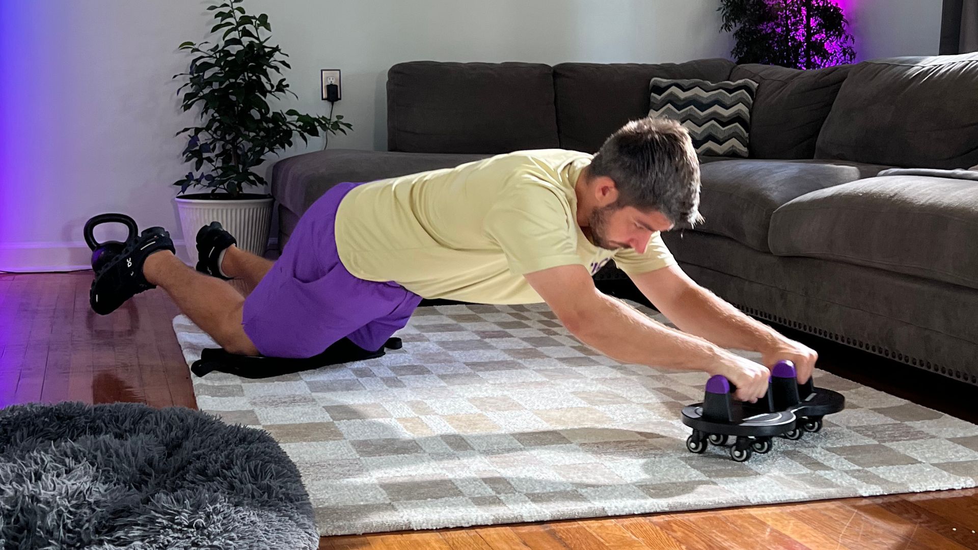 Man exercising with ab roller on a rug in a living room.