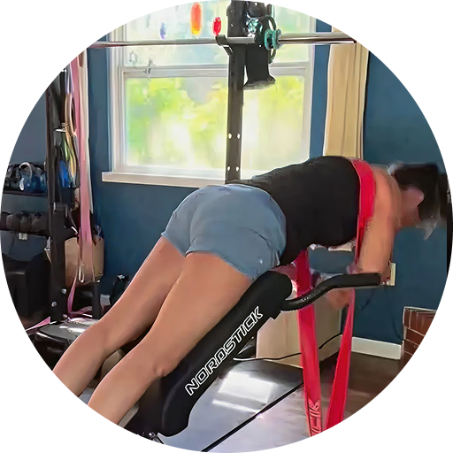 A woman in a home gym using a Nordstick exercise machine with a red resistance band.