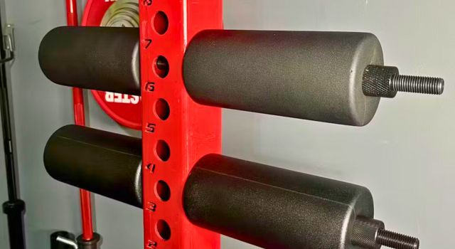 Red gym equipment with black padded rollers and numbered holes.