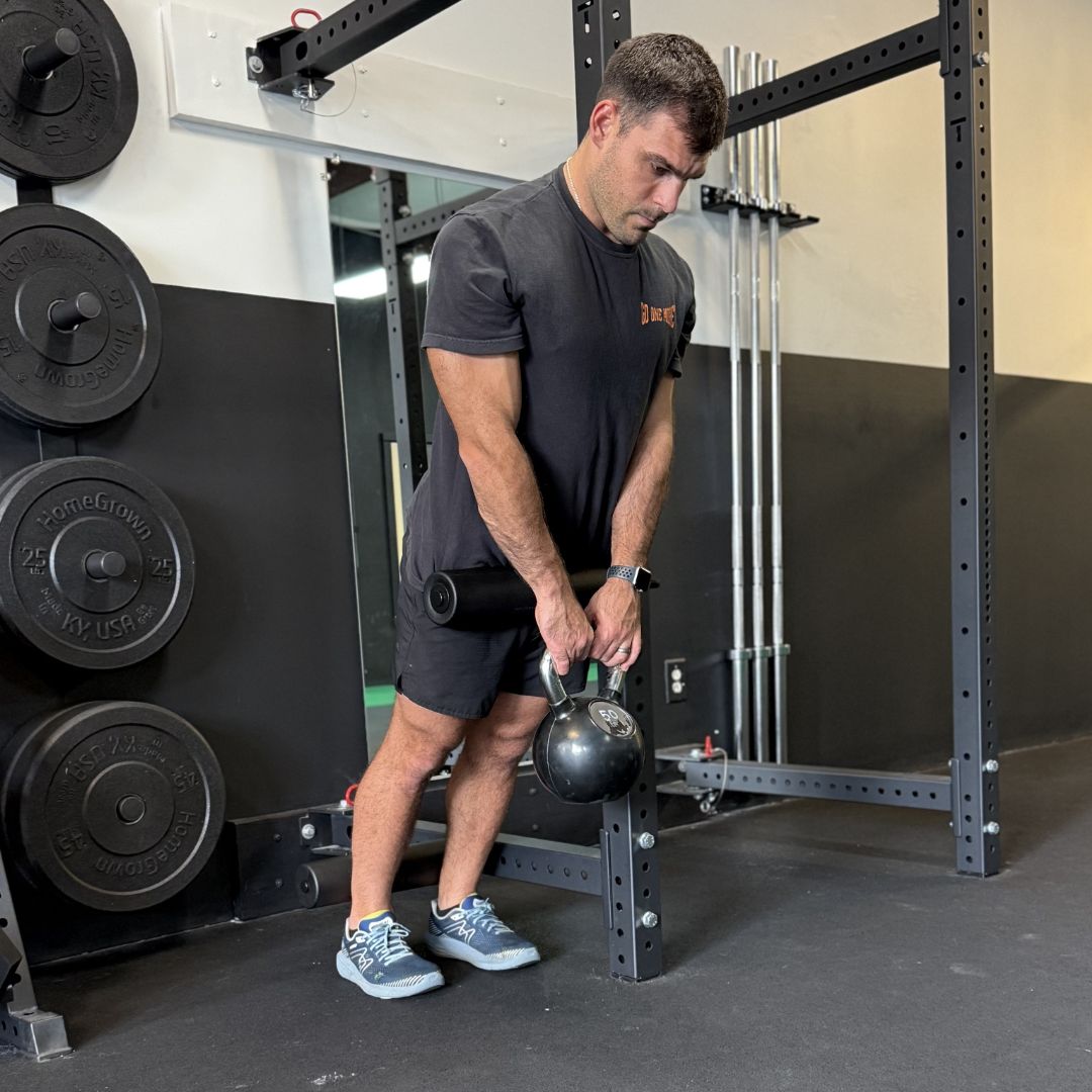 Man in gym lifting a kettlebell near weight rack.