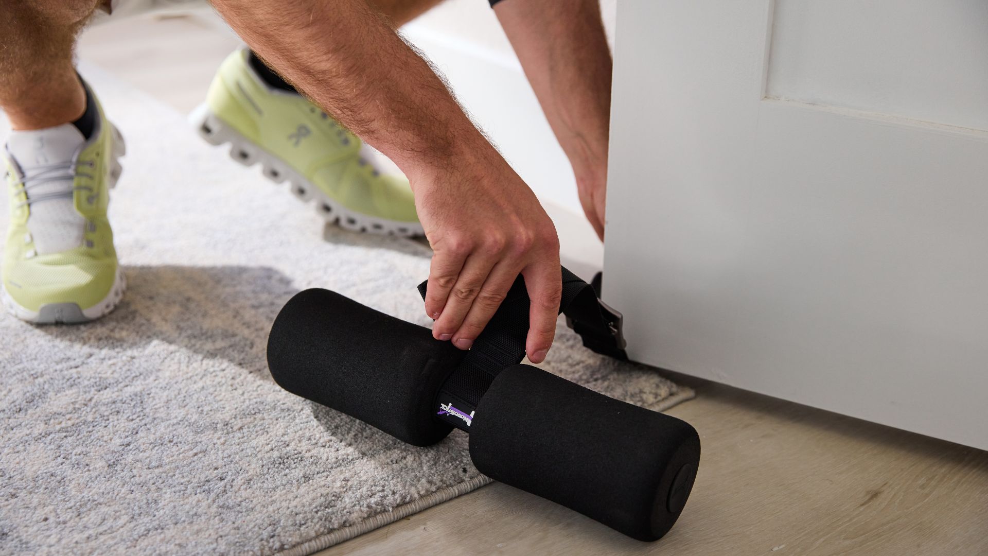 Person adjusting a foam roller under a door with light green sneakers visible.