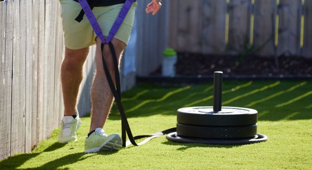 A person pulling a weighted sled on grass using a harness.
