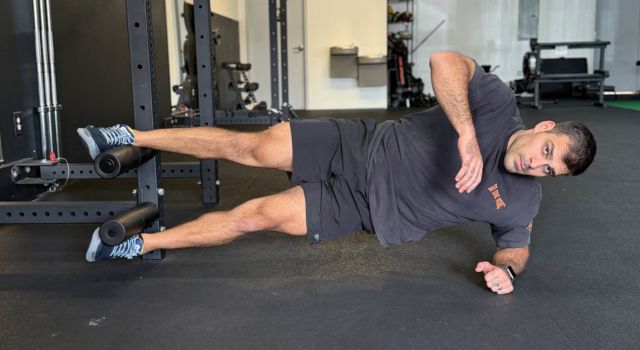 Man performing a side plank exercise in a gym.