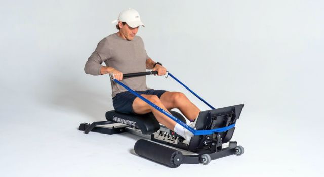 Person using a rowing machine with resistance bands in a studio setting.