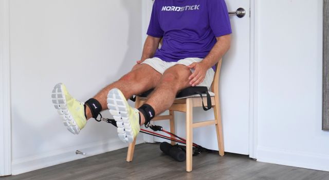 Person sitting on a chair using resistance bands for leg exercise.