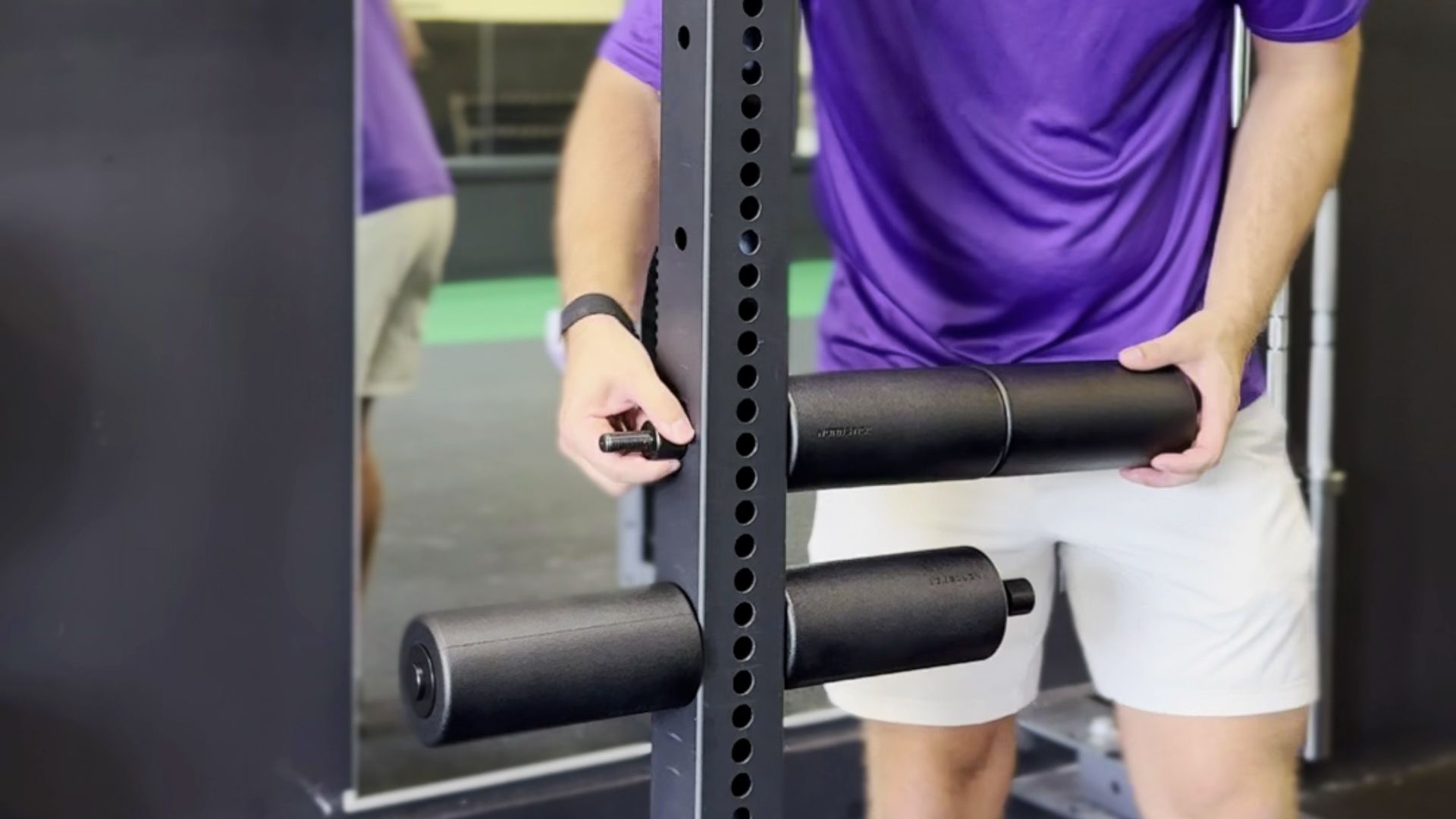 Person adjusting gym equipment with a black cylindrical attachment.