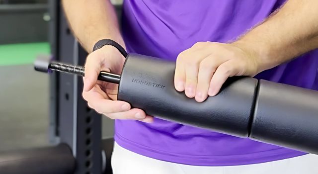 Person adjusting a black padded barbell pad in a gym setting.