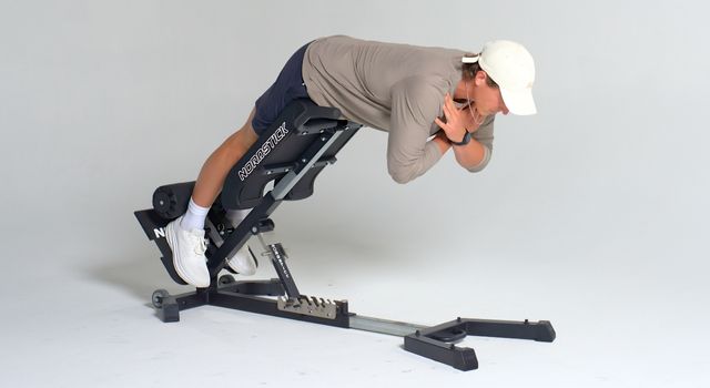 Person exercising on a hyperextension bench, wearing a cap and casual sportswear.