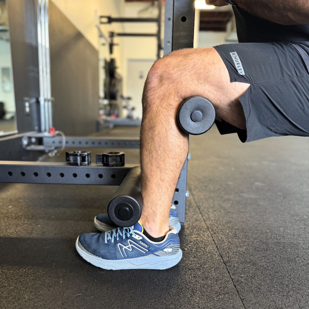 Person's leg in gym, using leg curl machine with blue sneakers.