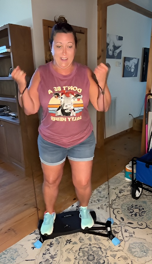 Person exercising on a stepping machine in a room, wearing a cow-themed shirt and shorts.