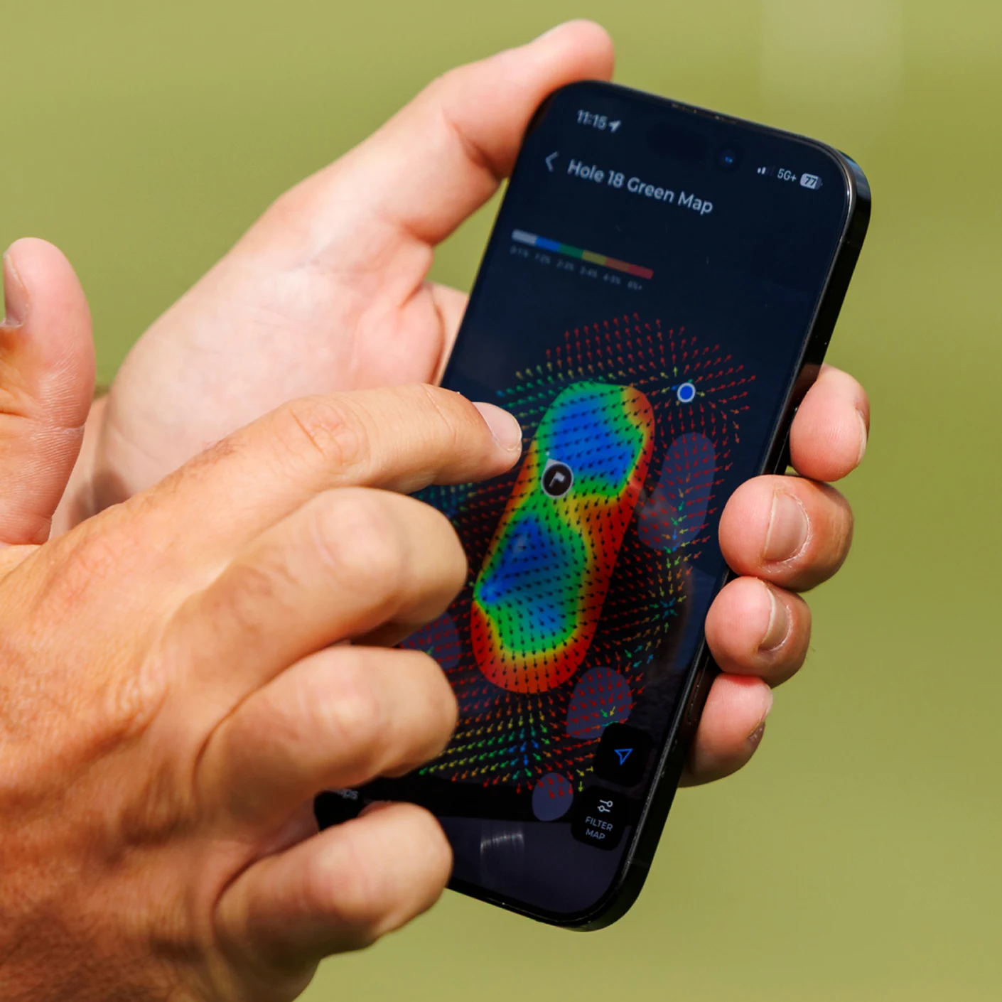 A person holding a smartphone that displays a colorful heat map of a golf green on its screen.