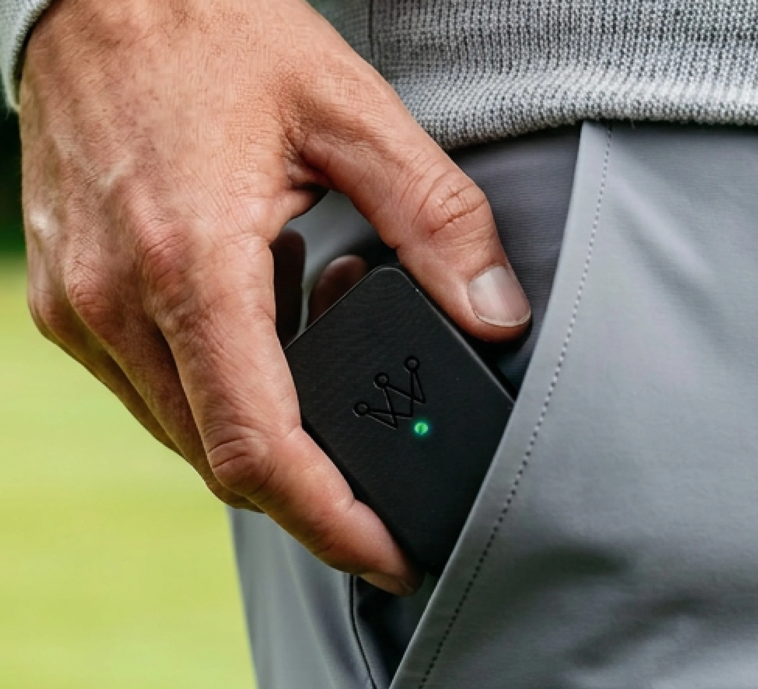 A close-up of a hand placing a small black electronic device with a crown logo into a pocket.