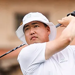 A man in a white bucket hat and white shirt swinging a golf club.