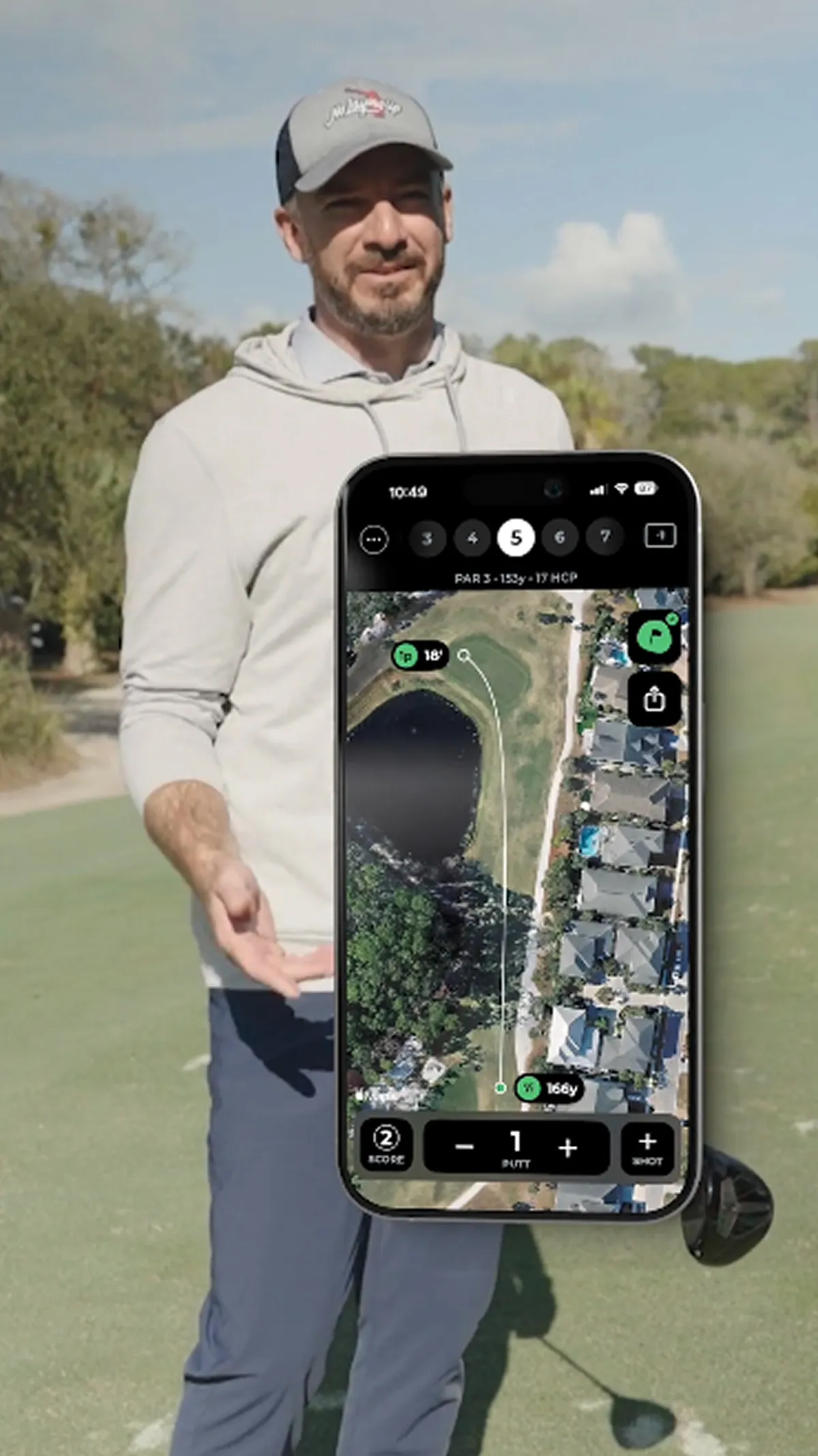 A man on a golf course holds a smartphone displaying a golf GPS app showing a hole layout.