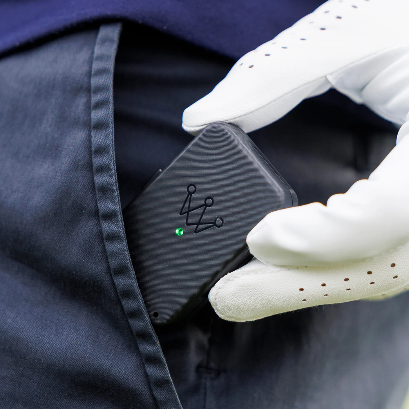 A person wearing a white golf glove places a small black electronic device into their pocket.