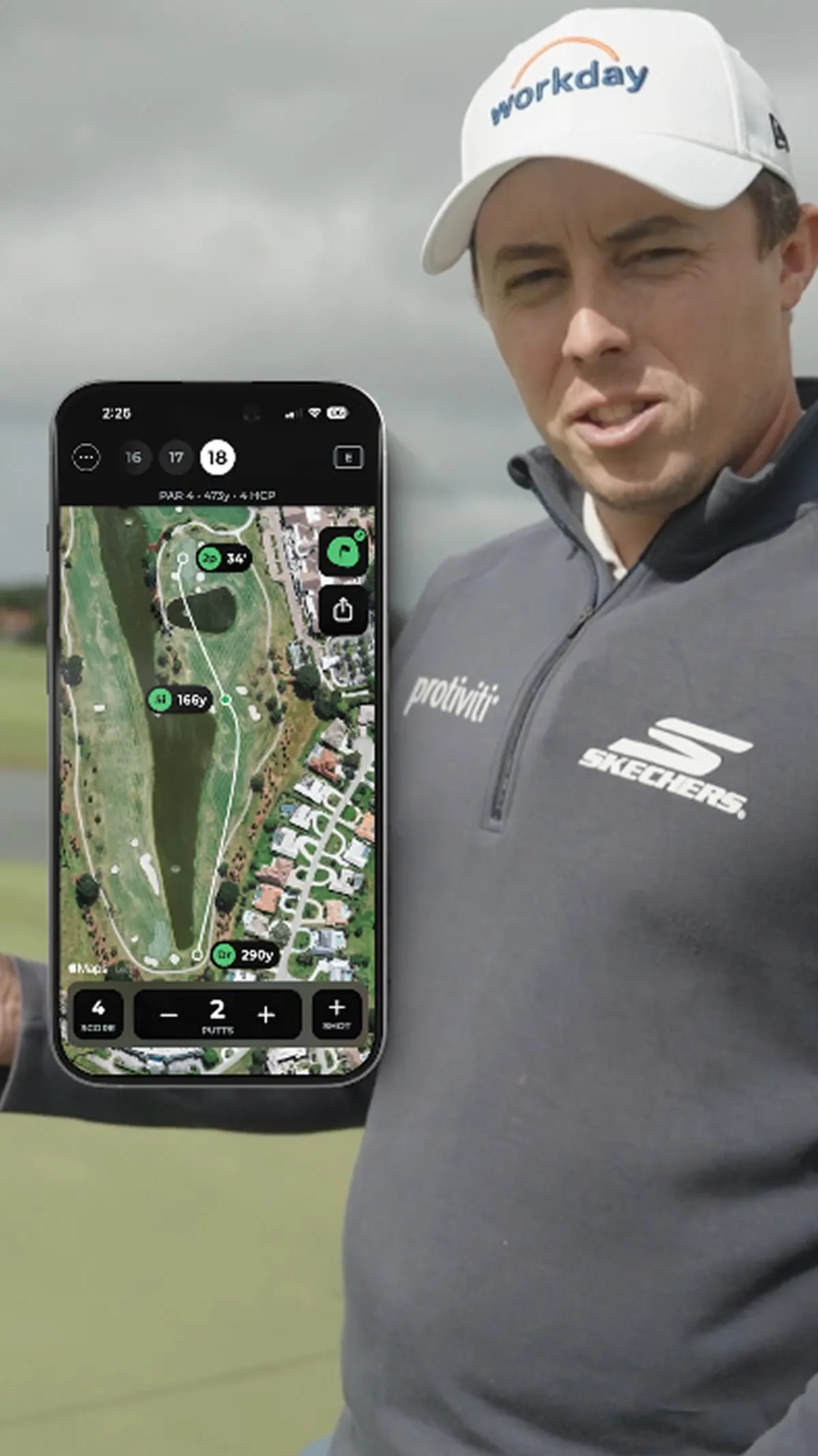 A male golfer in a grey pullover holds a smartphone displaying a golf course map app.