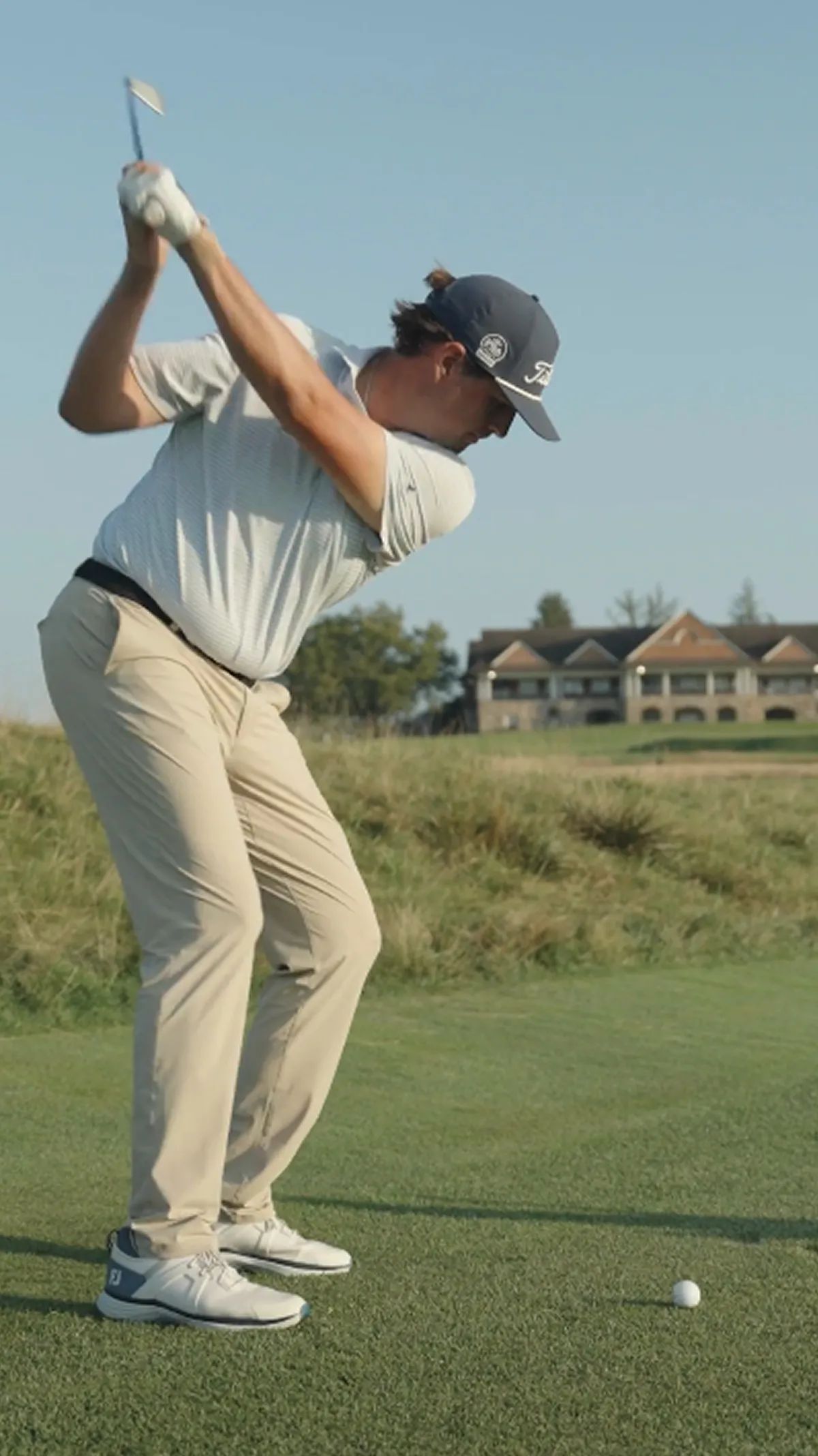 A man in mid-swing on a golf course, with a clubhouse in the background.