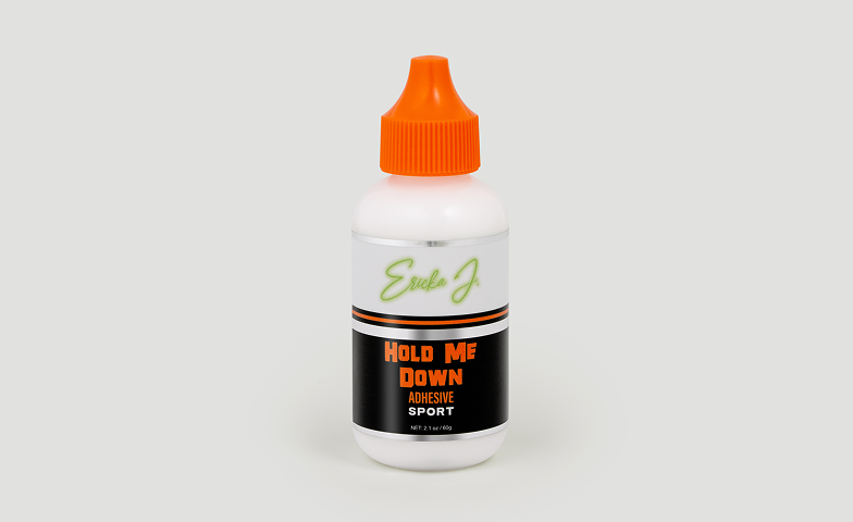 A white bottle of Ericka J. Hold Me Down Adhesive Sport with an orange cap against a plain background.