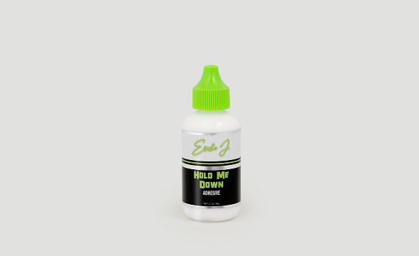 A white bottle of Eula J Hold Me Down Adhesive with a bright green cap against a grey background.