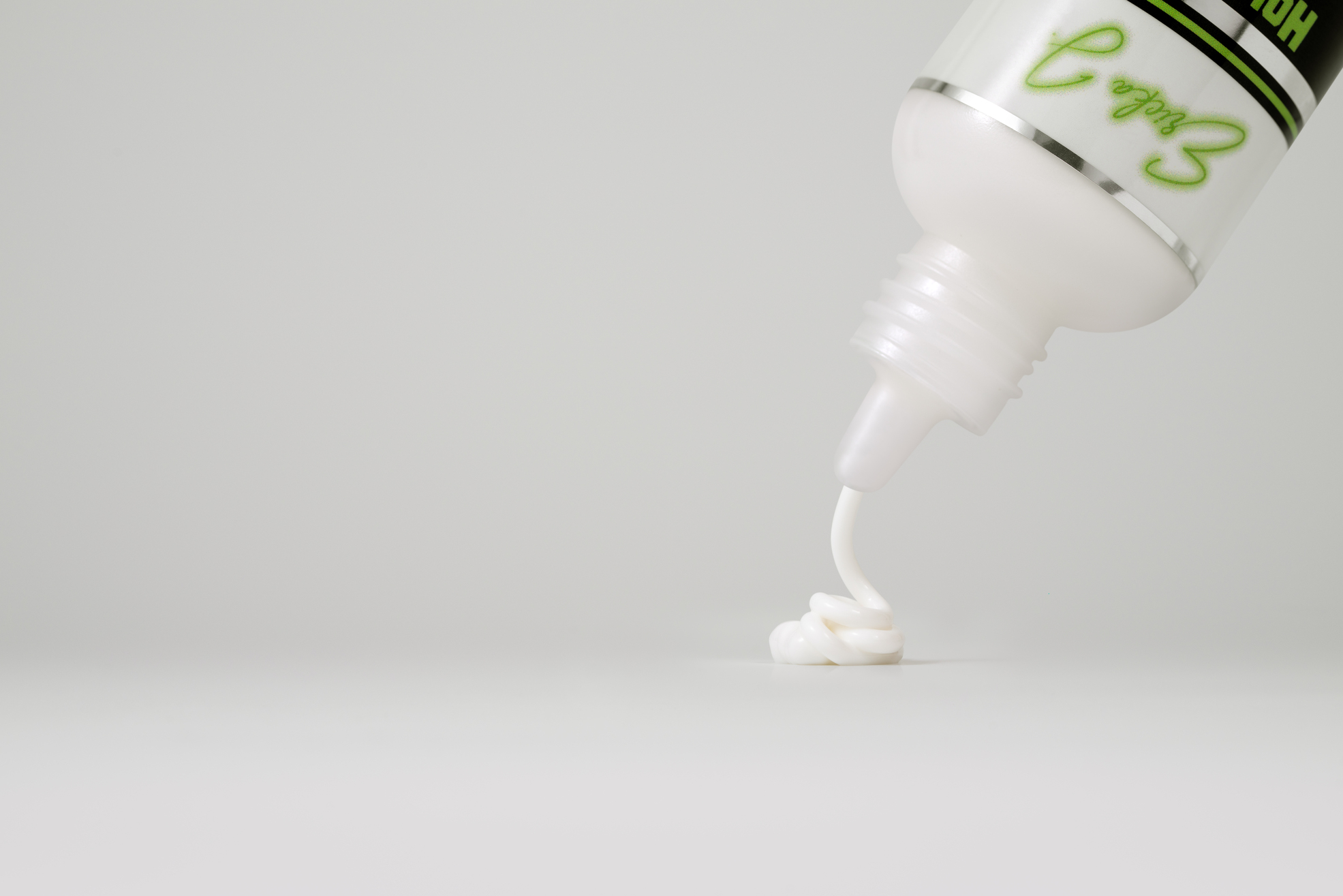 A white bottle of Ericka J. Hold Me Down Adhesive Sport with a bright green cap.