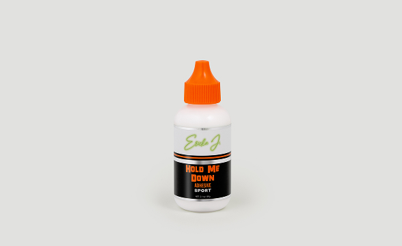 A white bottle of Ericka J. Hold Me Down Adhesive Sport with an orange cap on a plain background.