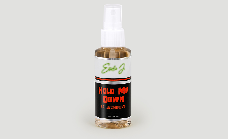 A clear spray bottle of Ericka J. 'Hold Me Down' Adhesive Skin Guard against a light grey background.