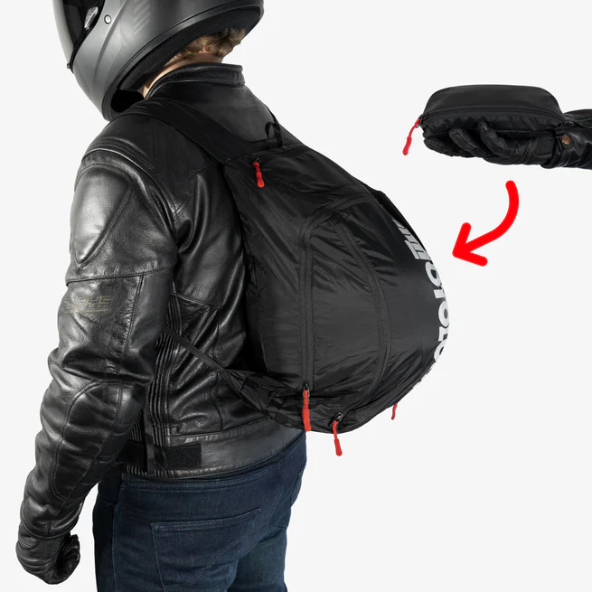 Person wearing a black motorcycle jacket and helmet with a large backpack.