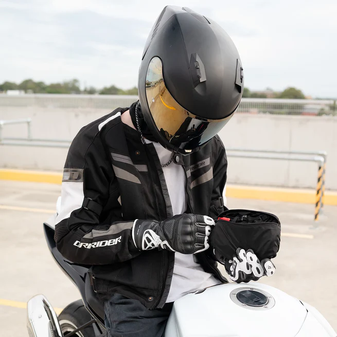 Person in motorcycle gear sitting on a bike, adjusting a small bag.