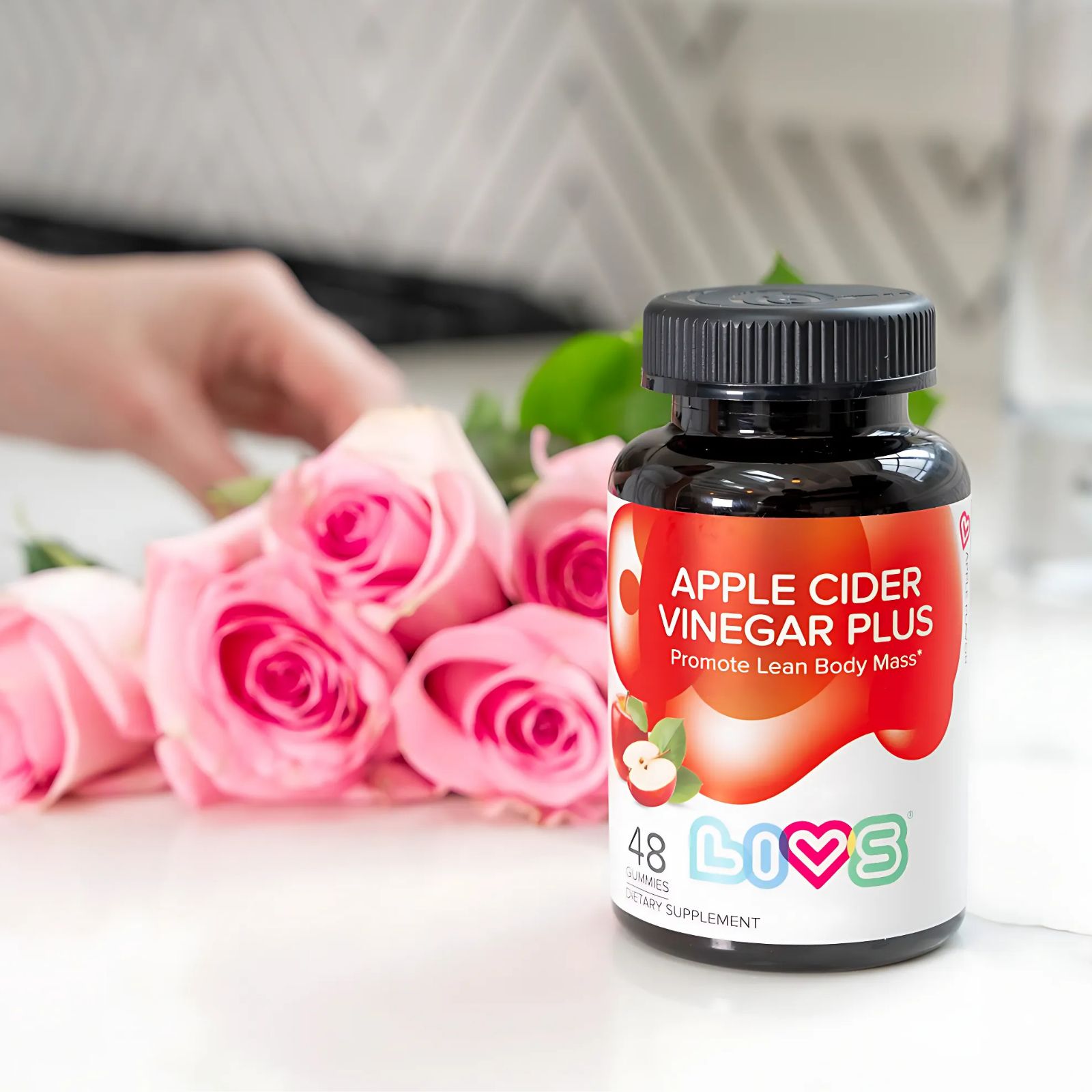 Bottle of apple cider vinegar gummies next to pink roses.