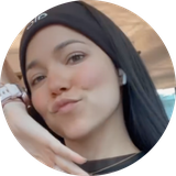 A close-up, circular photo of a young woman with a headband and earbud making a kissy face.