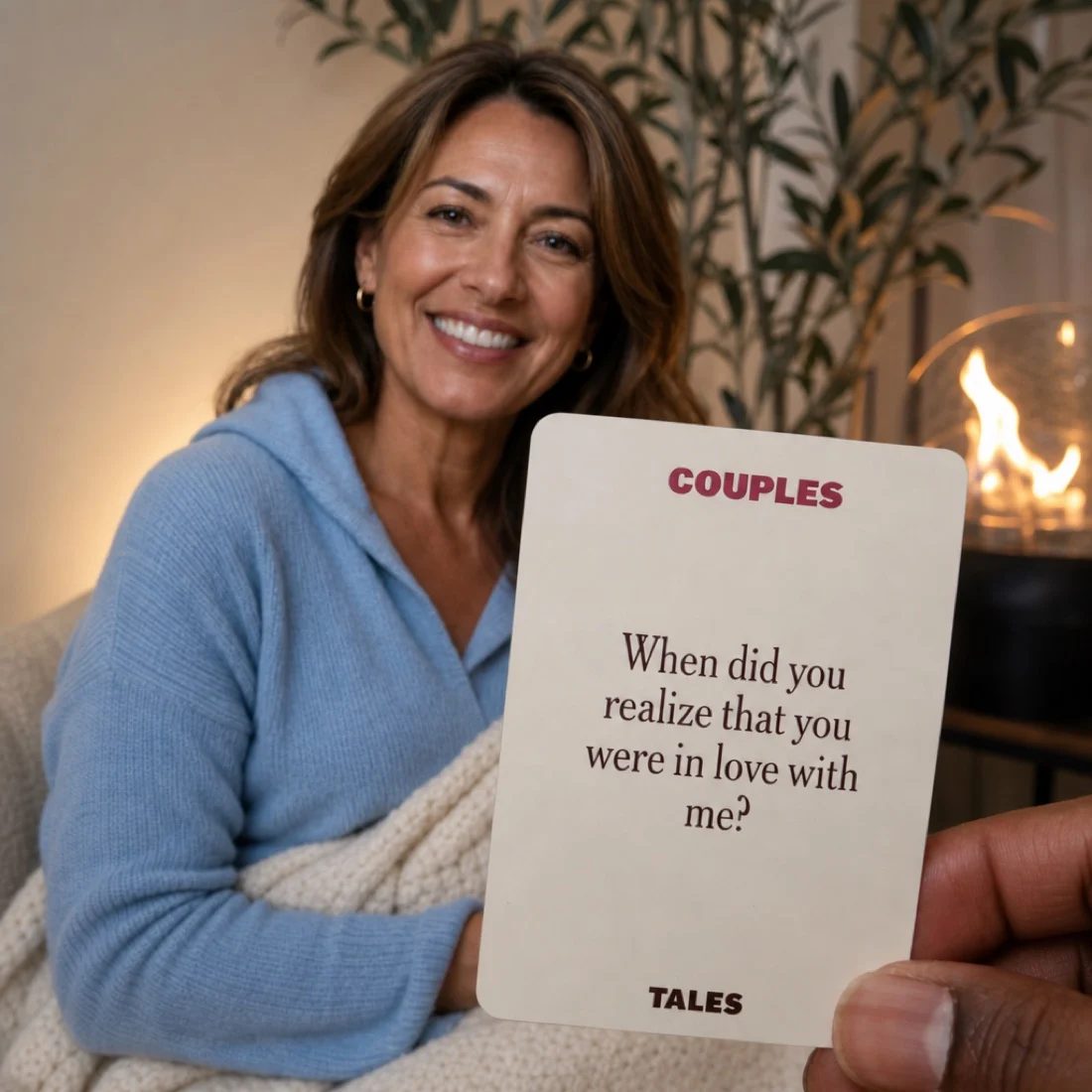 A hand holds a 'Couples' game card towards a smiling woman sitting on a couch.