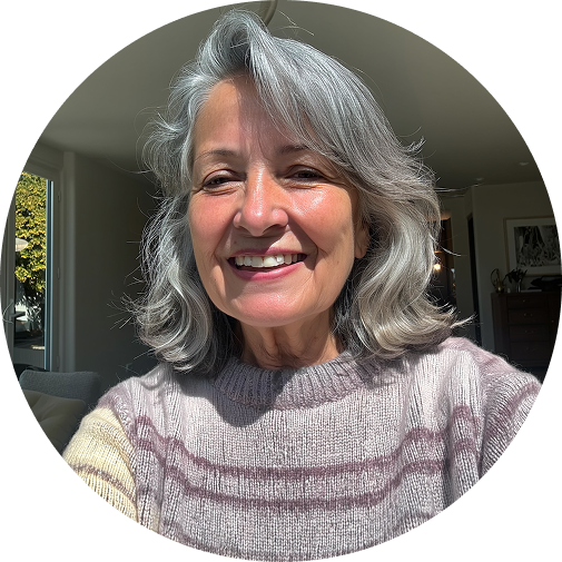 Smiling person with gray hair and a sweater in a bright room.