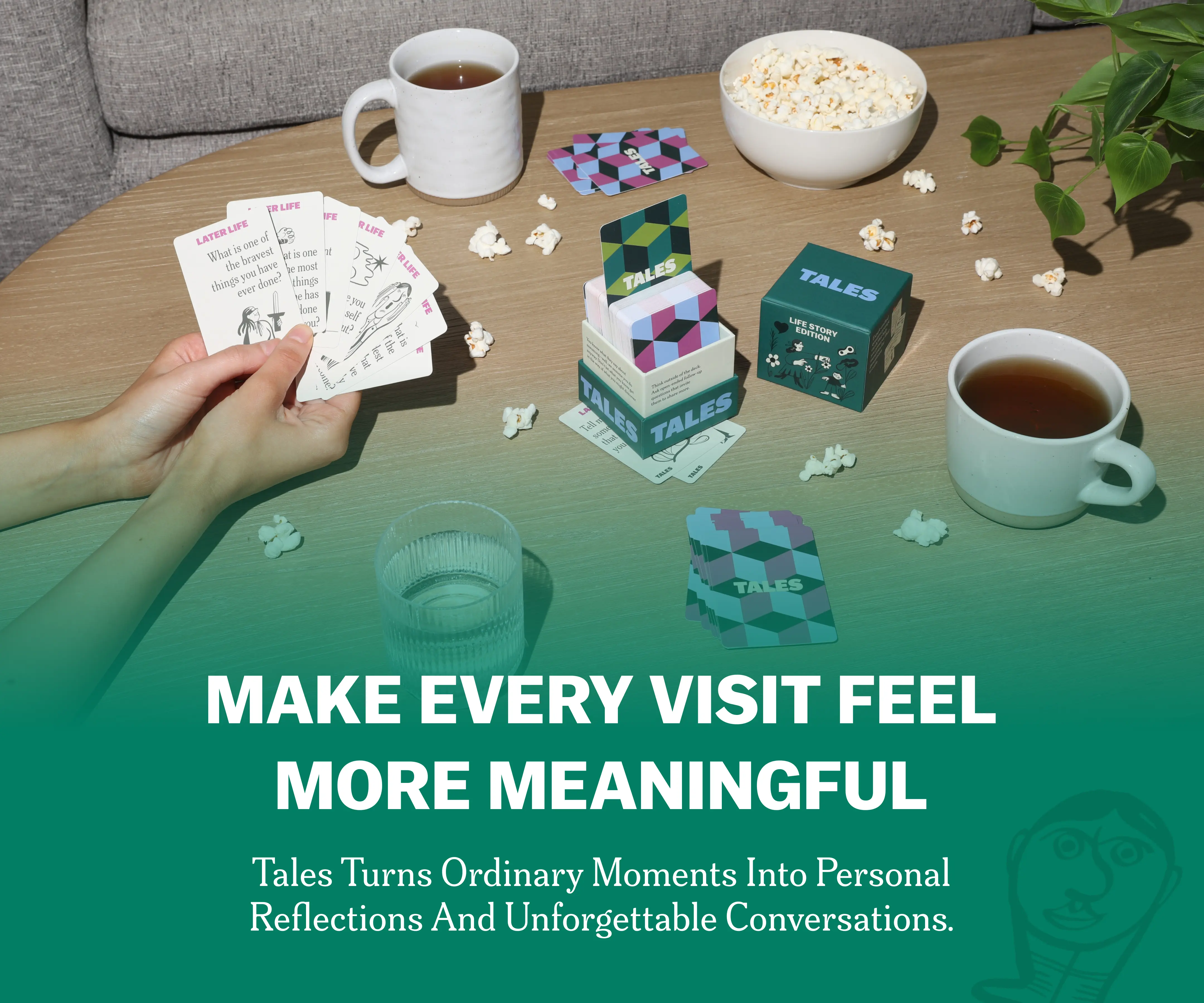 Hands holding cards, tea, popcorn, and a card game on a table.