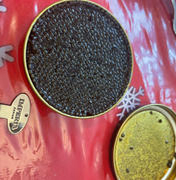 Open tin of caviar on a festive red surface with snowflake decoration.