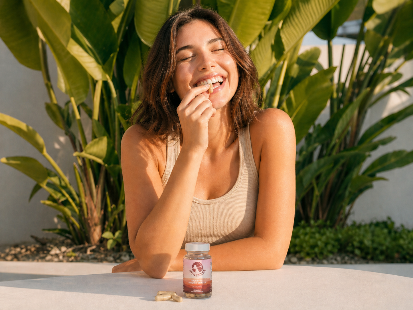 A smiling woman with her eyes closed puts a capsule in her mouth, sitting at an outdoor table.